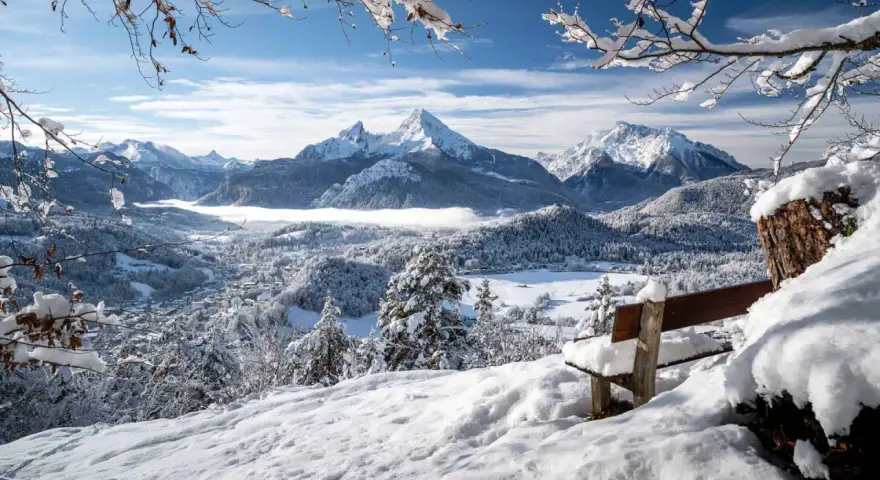 Ein verschneites Tal mit einem majestätischen Berg im Hintergrund. Eine Bank lädt zum Verweilen ein, perfekt für einen **ausflug im winter**.