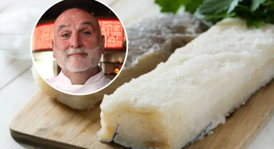 Chef sonriente junto a trozos de bacalao en salazón sobre tabla de madera.