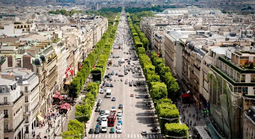 Vista aérea de la **Champs-Élysées** en París, con tráfico y peatones paseando entre los árboles y edificios.