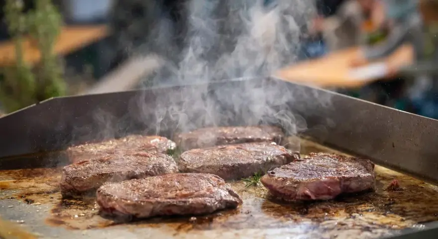 Mehrere saftige Rumpsteaks braten auf einer heißen Platte, Dampf steigt auf.