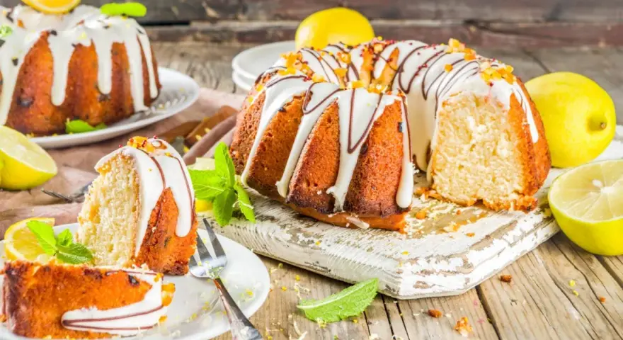 Najlepsza babka cytrynowa wilgotna na oleju, ozdobiona lukrem i skórką cytrynową, z kawałkami na talerzykach.