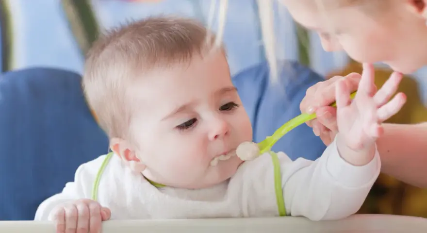Mama karmi dziecko łyżeczką do karmienia niemowląt. Maluch z zaciekawieniem patrzy na jedzenie.