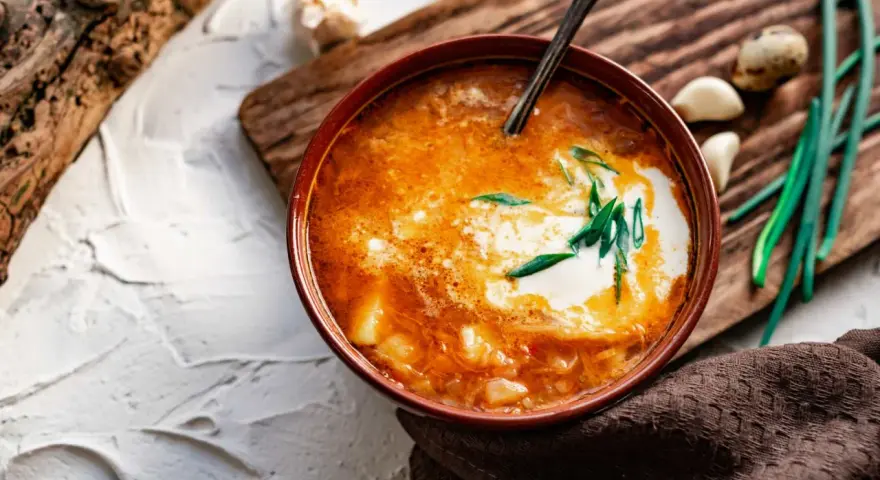 Un tazón de sopa de ajo con crema y cebolleta, acompañado de ajos y cebolletas.