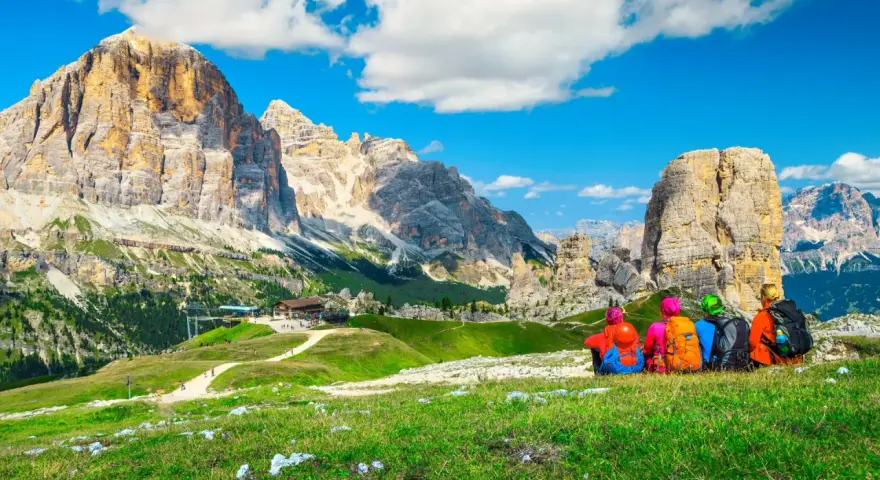 Quattro escursionisti ammirano un maestoso itinerario dolomiti, con cime imponenti e un rifugio alpino.