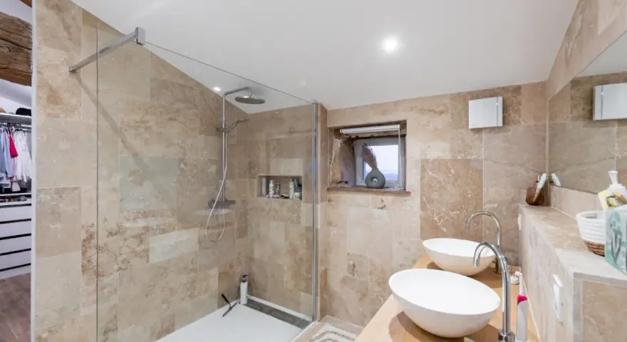 Salle de bain moderne avec douche à l'italienne, double vasque et carrelage en pierre naturelle. Un projet réussi pour refaire la salle de bain.