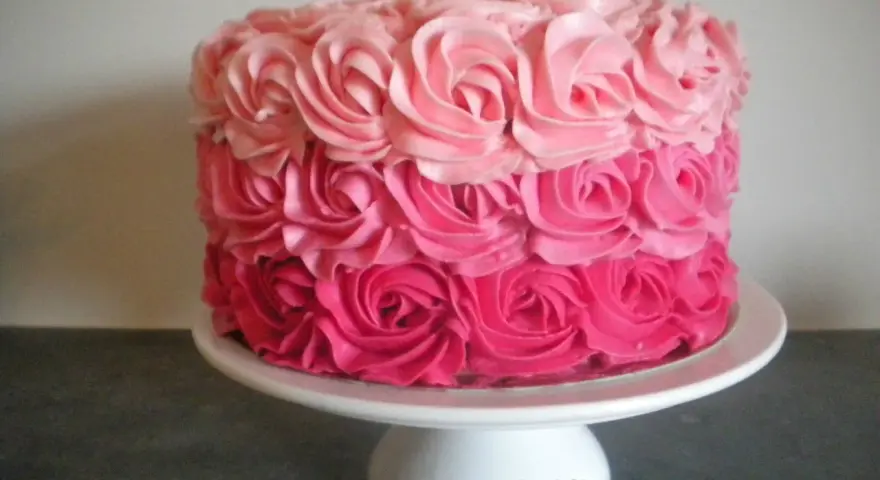 Gâteau rond décoré de roses en crème rose, du plus foncé au plus clair. Un délice visuel !