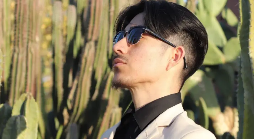 Uomo con abito beige e camicia nera, occhiali da sole, tra i cactus. Un look elegante per ogni occasione.