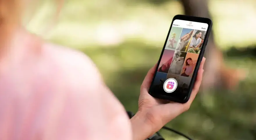Osoba trzyma telefon z widokiem na ekran Instagrama, gdzie widać siatkę zdjęć i ikonę Reels. Dowiedz się, jak zrobić rolkę na Instagramie ze zdjęć.