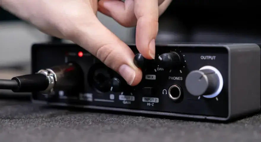 Dłoń reguluje pokrętło miksu na interfejsie audio, przygotowując wyjście liniowe do pracy.