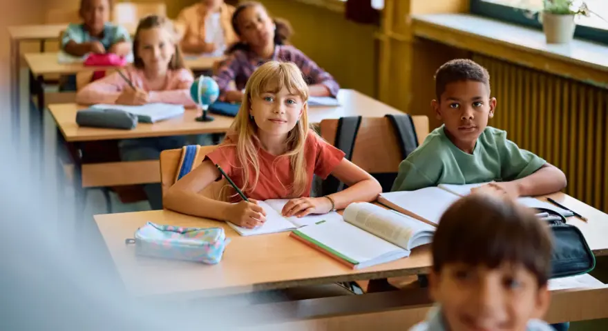 Dzieci w klasie skupione na lekcji. Uczennica pisze w zeszycie, obok niej leży piórnik. To pokazuje, co na koncentrację u dzieci: nauka i zaangażowanie.