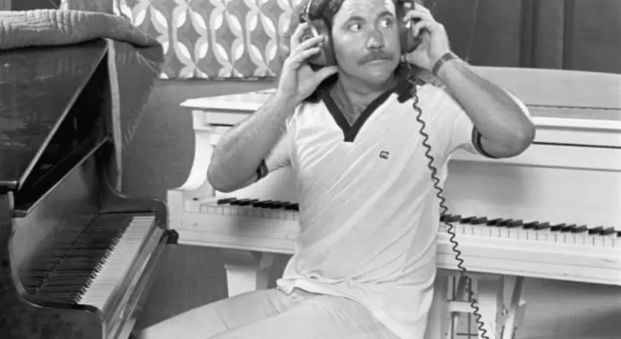 Billy Powell hört mit Kopfhörern Musik, während er neben einem Klavier sitzt.
