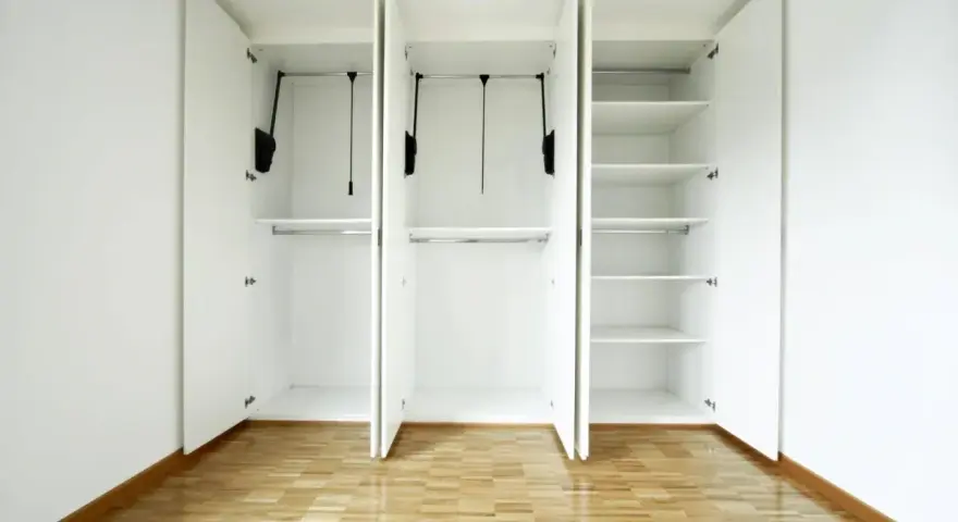 Interno di un armadio bianco a tre ante, vuoto, con ripiani e barre appendiabiti. Un esempio di come costruire un armadio funzionale.