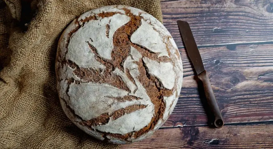 Pan casero rústico sobre arpillera, listo para cortar con un cuchillo. Una delicia para tu receta de pan casero.