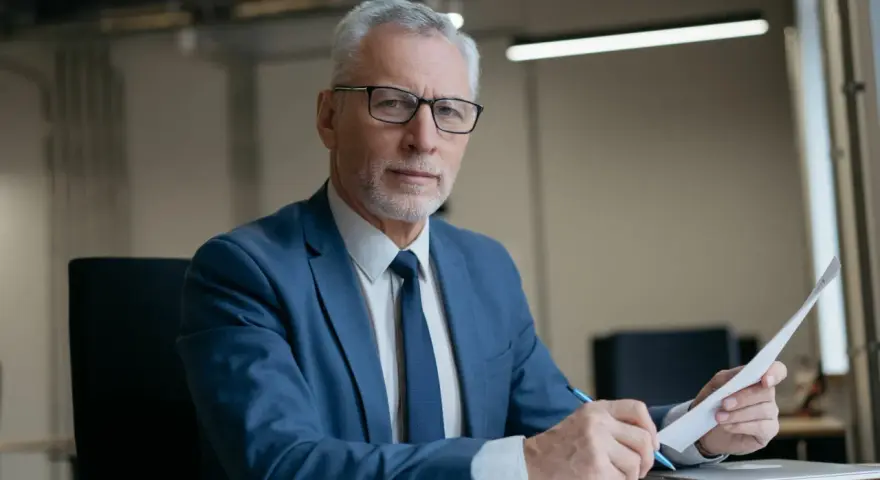 Poważny mężczyzna w garniturze analizuje dokumenty, zastanawiając się, ile komornik może zabrać z 13 pensji.