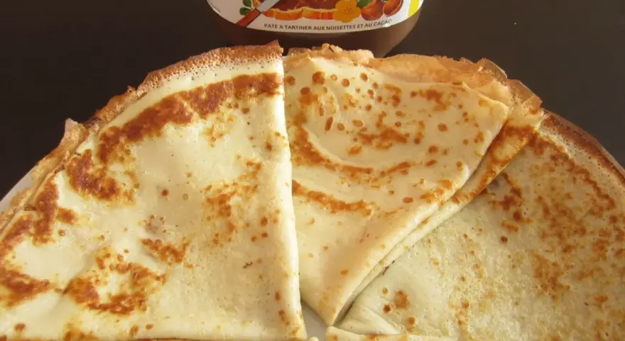 Crêpes dorées prêtes à être garnies, avec un pot de Nutella en arrière-plan. Une recette facile pour des crêpes maison !