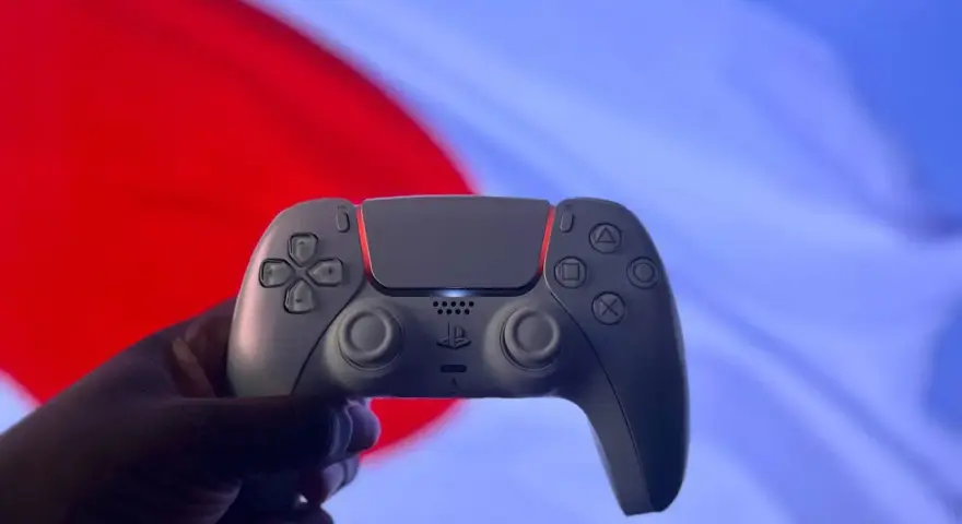 Dłoń trzyma biały kontroler DualSense. Czy gry z PS5 działają na PS4? To pytanie nurtuje graczy.