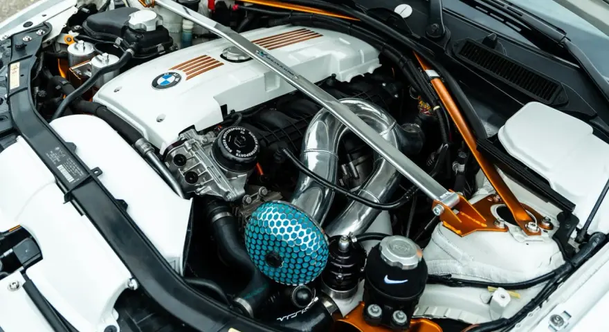 Custom BMW engine bay with a silver strut bar and orange accents. If your engine is ticking, check the oil level and listen for unusual noises.