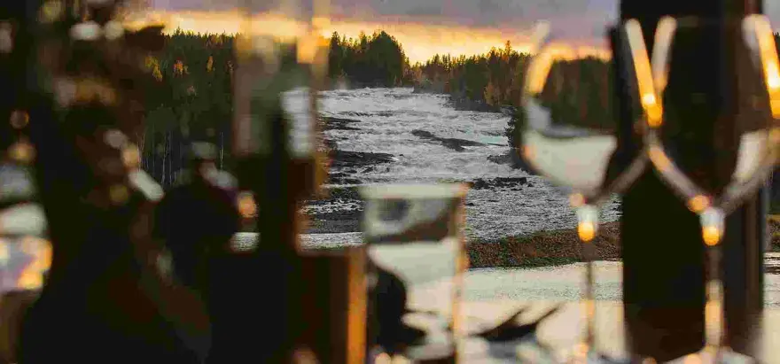 Storforsen camping: en brusande fors i solnedgången, med skog och träd som ramar in. Mysig belysning i förgrunden.
