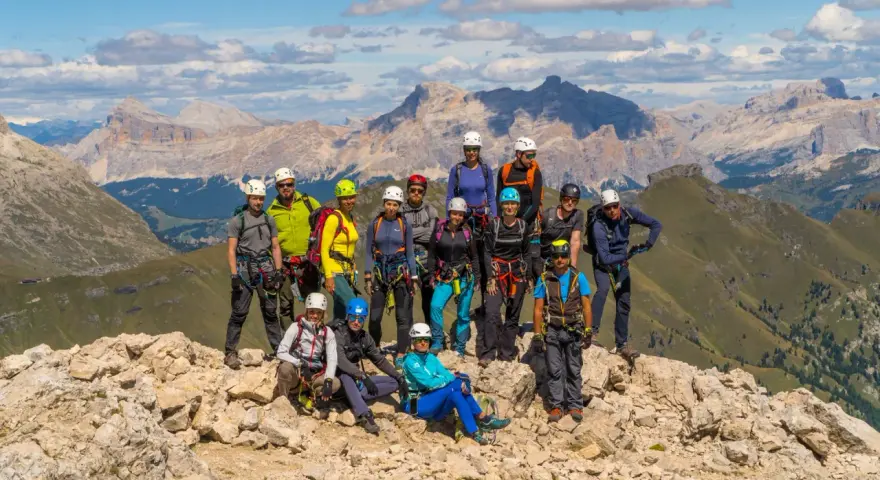 Grupa turystów w sprzęcie wspinaczkowym pozuje na tle górskich krajobrazów Dolomitów. To wspaniała przygoda na via ferrata Dolomity!