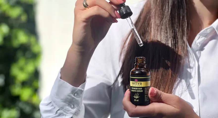Kobieta trzyma buteleczkę z olejkiem Sattva i pipetkę z serum do włosów.