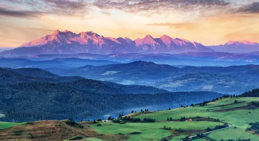 Tatry o zachodzie słońca, jedno z **10 najpiękniejszych miejsc w Polsce**. Góry w odcieniach różu i fioletu, zielone wzgórza i lasy.