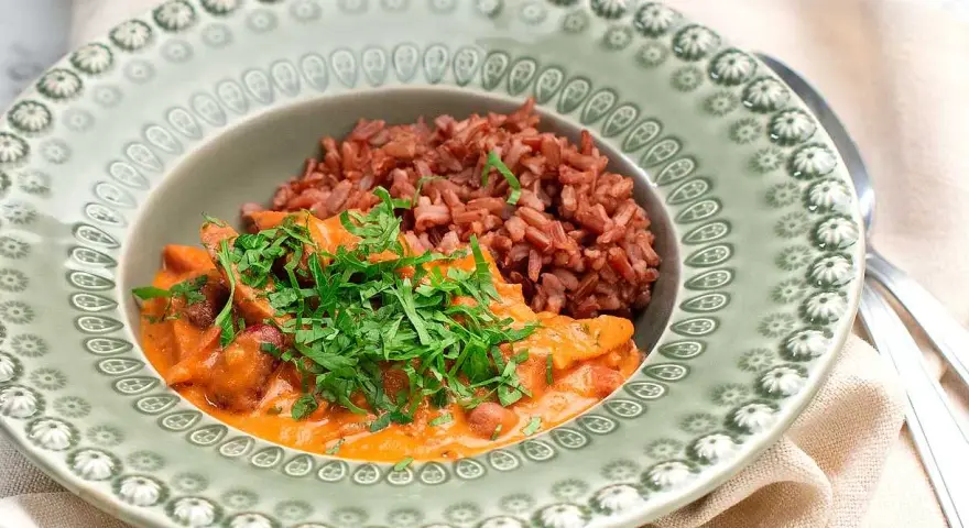 En portion korv stroganoff med rött ris, toppad med färsk persilja, serveras på en vacker grön tallrik.
