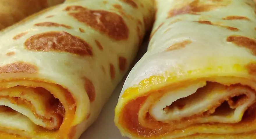 Dwa zwinięte naleśniki z dżemem, apetycznie wyglądające, z widocznym pomarańczowym nadzieniem.