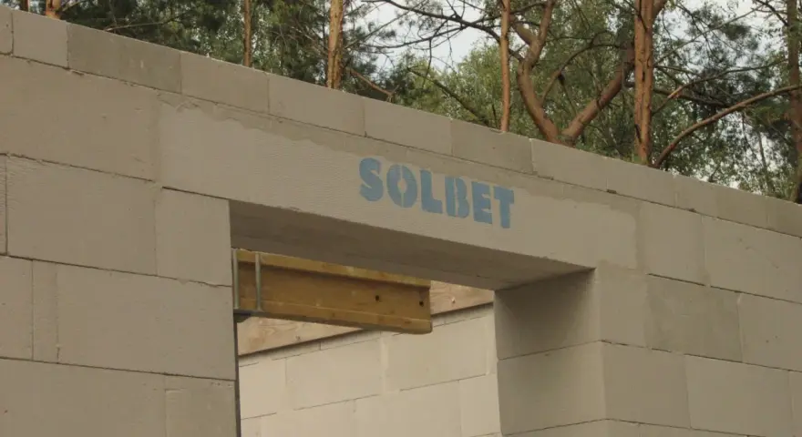 Ściana z bloczków betonowych z widocznym nadprożem marki SOLBET. Widać, jak nadproże ile powinno zachodzić, by zapewnić stabilność konstrukcji.