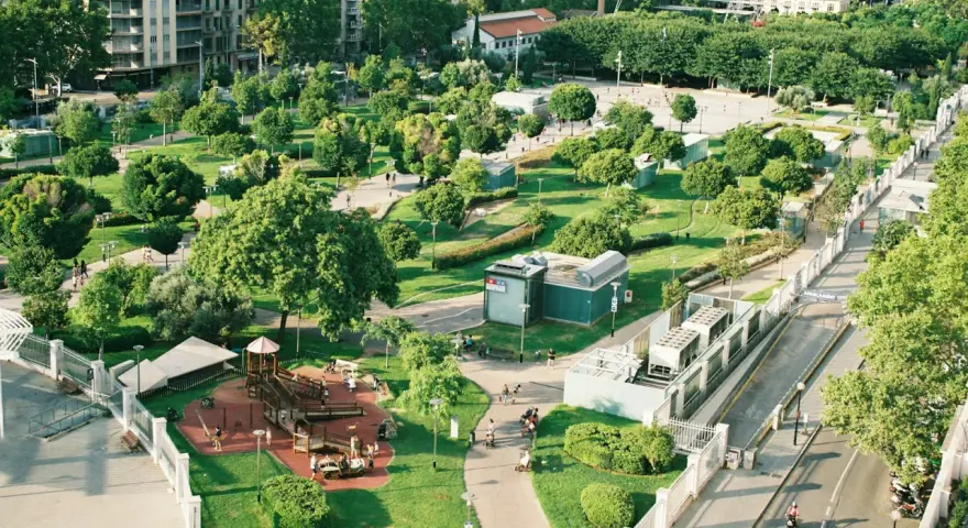Park z placem zabaw i alejkami, otoczony budynkami. Wygląda jak jeden z najbardziej zielonych miast w Polsce.