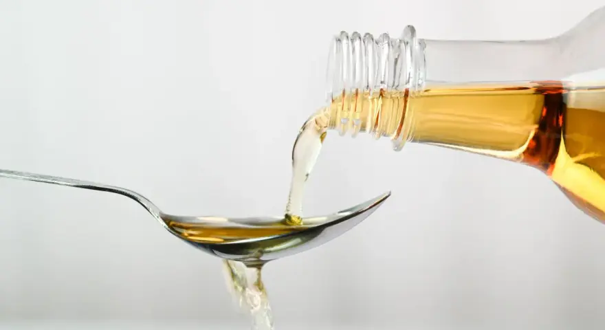 Apfelessig wird aus einer Flasche auf einen Löffel gegossen. Ein Tropfen für das Abnehmen.