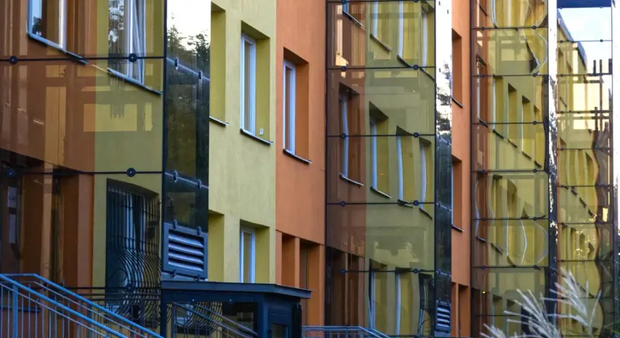 Nowoczesny blok z żółtymi i pomarańczowymi elewacjami, przeszklonymi klatkami schodowymi. Czy ustawa o windach wymusi montaż dźwigów w niskich blokach z czwartego piętra?