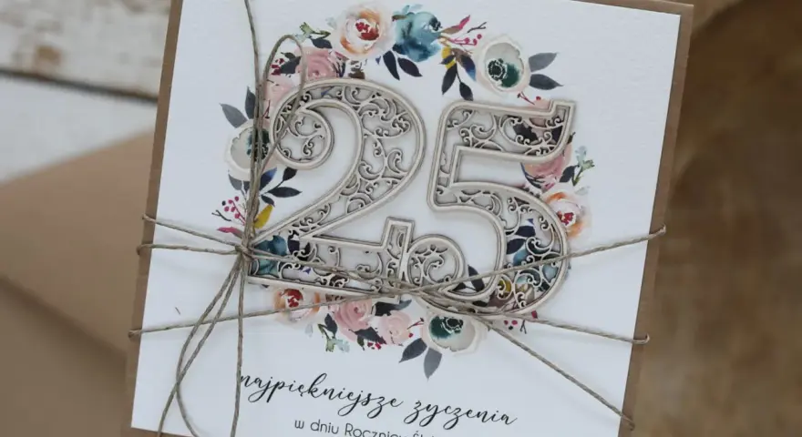 Elegancka kartka z napisem "25 lat małżeństwa jakie to gody", ozdobiona kwiatami i ażurową liczbą 25.