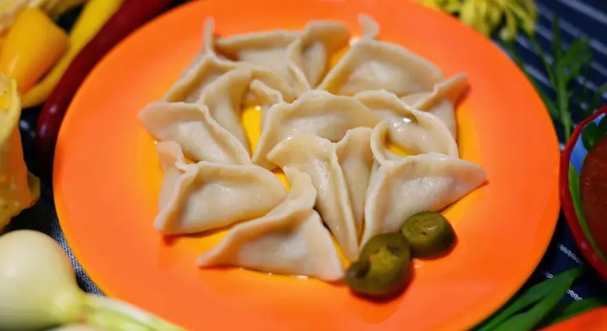 Pyszne pierogi meksykańskie, ułożone na pomarańczowym talerzu, z dodatkiem jalapeño i sosu.