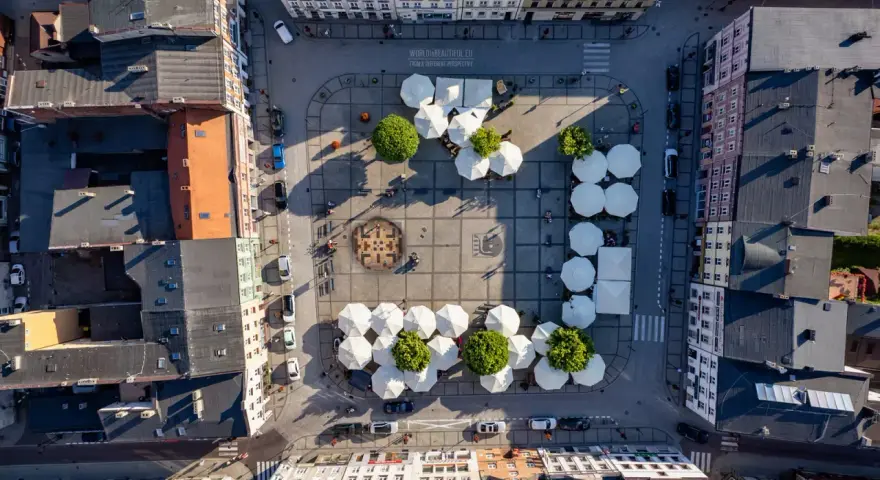 Widok z lotu ptaka na rynek w Kościerzynie, z białymi parasolami i zielenią.