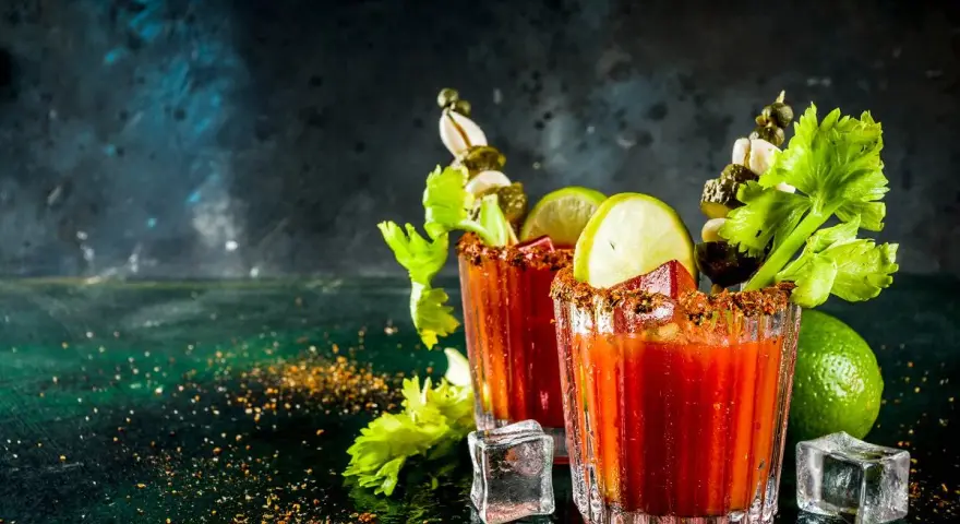 Dwa drinki Bloody Mary, ozdobione łodygami selera, limonką i piklami. Ich historia jest równie intrygująca, co smak.
