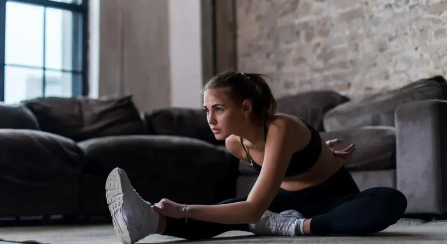 Młoda kobieta w sportowym stroju wykonuje ćwiczenia rozciągające na podłodze. Widać, co daje rozciąganie po treningu: poprawia elastyczność i relaksuje.