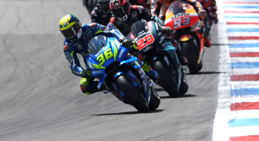Pilotos de **MotoGP hoy** compiten en una carrera emocionante. El piloto con el número 36 en su Suzuki lidera, inclinado en una curva cerrada.