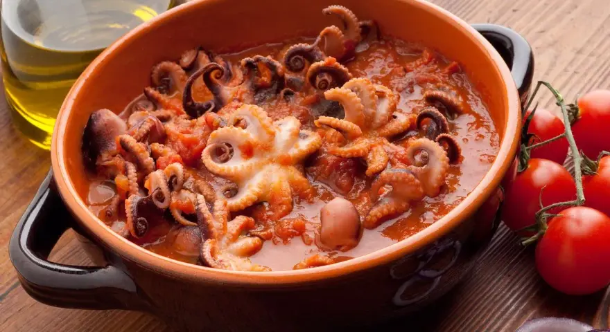 Polipetti in purgatorio, un piatto succulento con tentacoli che danzano in un sugo rosso, accompagnati da pomodorini freschi e cipolla.