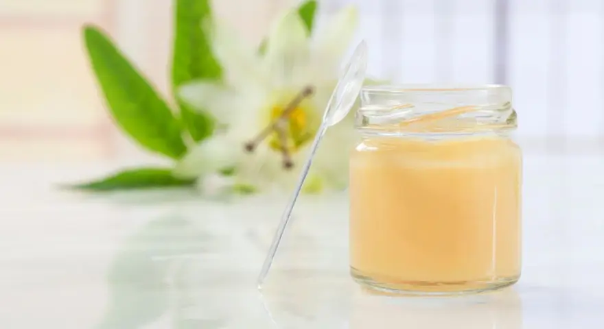 Un vasetto di pappa reale, con un fiore sullo sfondo. Alcuni credono che la pappa reale fa ingrassare, ma è un alimento nutriente.
