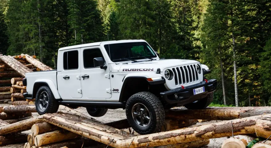 Biały jeep pickup Rubicon pokonuje przeszkodę z bali drewna w lesie.