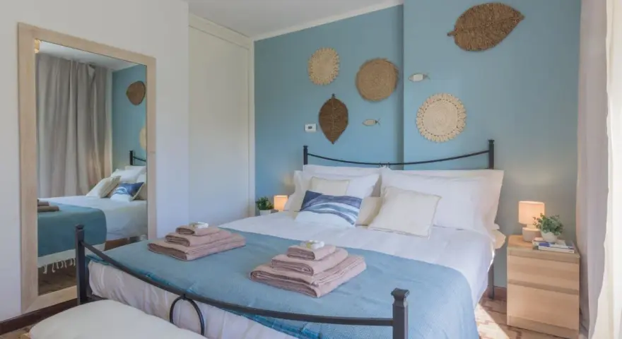 Idee camera da letto: letto matrimoniale con biancheria azzurra e cuscini bianchi, decorazioni a forma di foglia e pesci sulla parete blu.