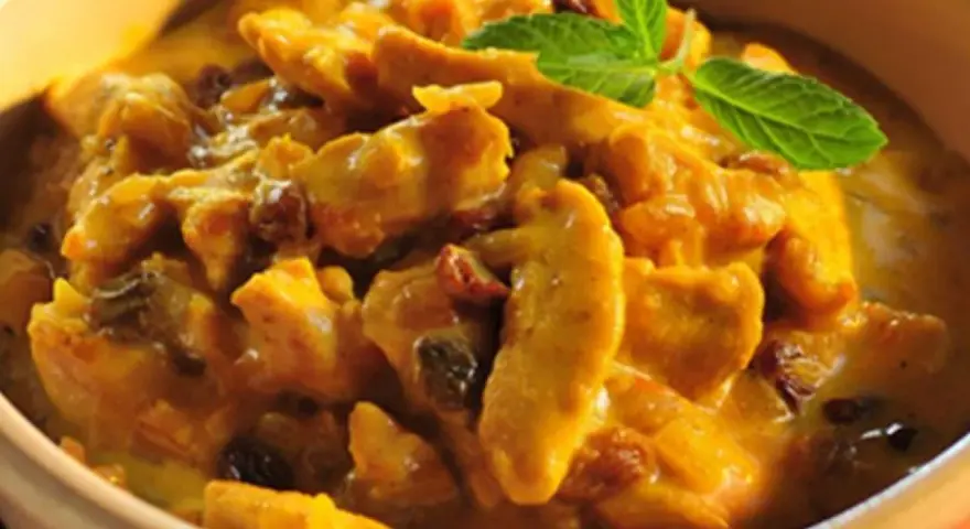 Pyszny kurczak w sosie curry z rodzynkami, ozdobiony listkiem mięty. Idealny przykład, jak zrobić sos curry do kurczaka.