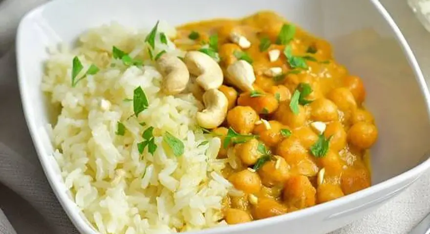 Curry de garbanzos cremoso con arroz blanco y anacardos en un cuenco blanco.