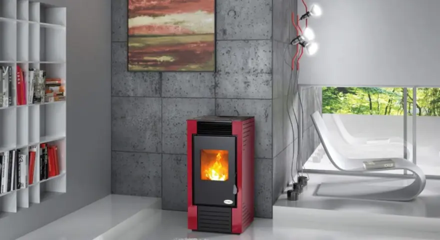 Estufa roja moderna con fuego encendido, mostrando cómo funciona la biomasa. Estantería blanca con libros y sillones blancos al fondo.