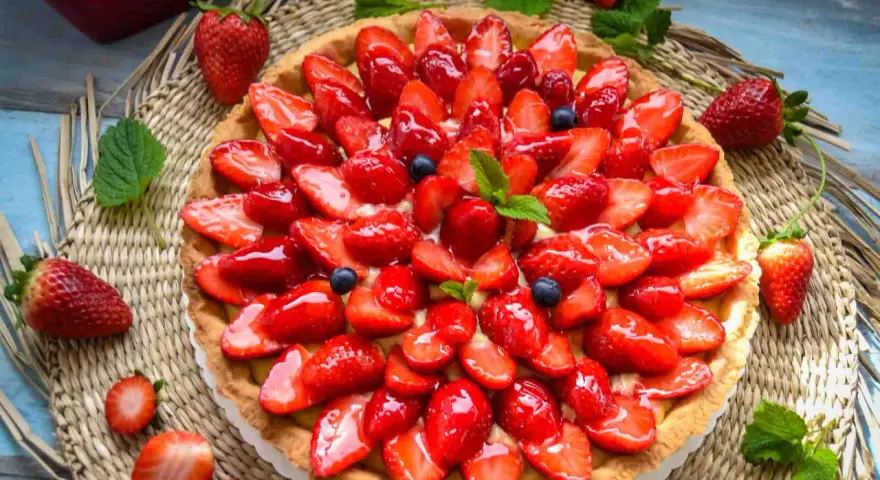 Ein leckerer Erdbeerkuchen mit einem wunderschönen Muster aus frischen Erdbeeren und Blaubeeren, glasiert und garniert mit Minze.