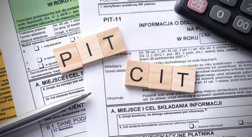Drewniane klocki z literami "PIT" i "CIT" na formularzu podatkowym. Temat: podatek od sprzedaży nieruchomości po upływie 5 lat.