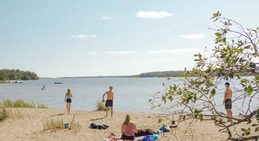 Solig dag vid Hallmare havsbad. Människor njuter på stranden, badar och leker i vattnet.