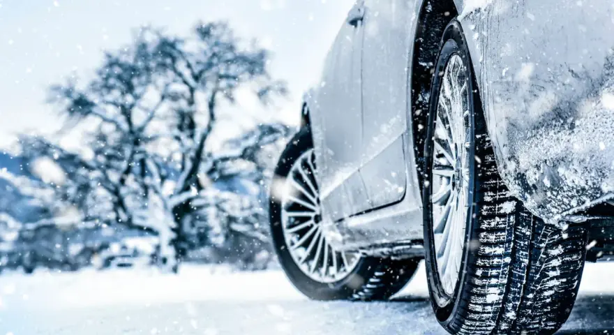 Auto im Schnee mit Winterreifen, verschneiter Baum im Hintergrund.