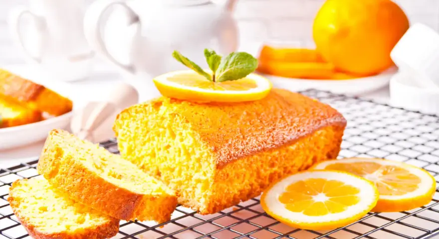 Un soffice plumcake al limone, guarnito con una fetta d'arancia e menta, su una griglia, pronto per essere gustato.