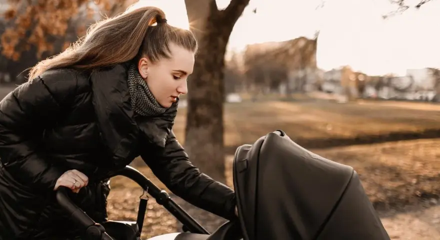 Mama przygotowuje malucha na spacer w 15 stopniach. Ciepła kurtka i szalik to podstawa, by zapewnić komfort dziecku w wózku.